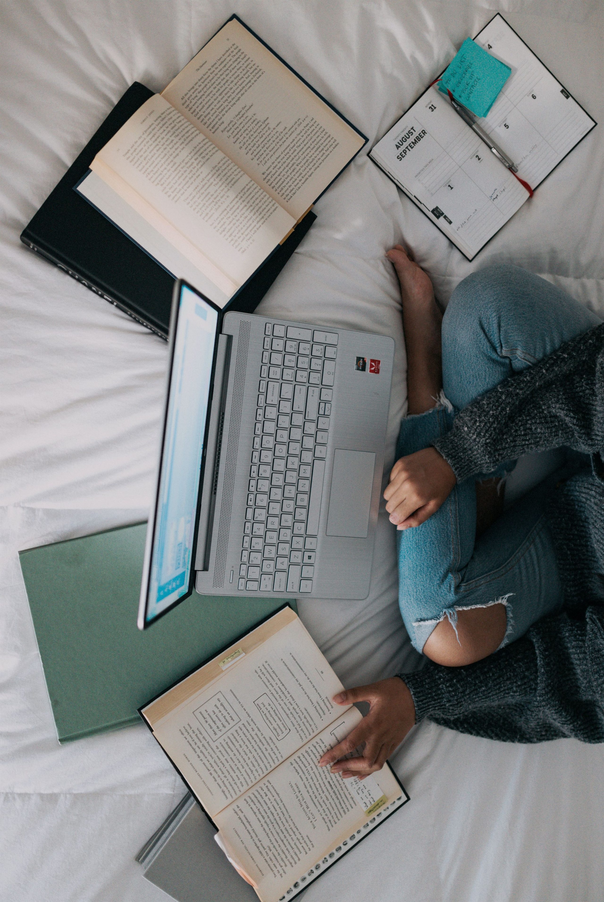 une femme assise sur un lit avec un ordinateur portable et des livres.
